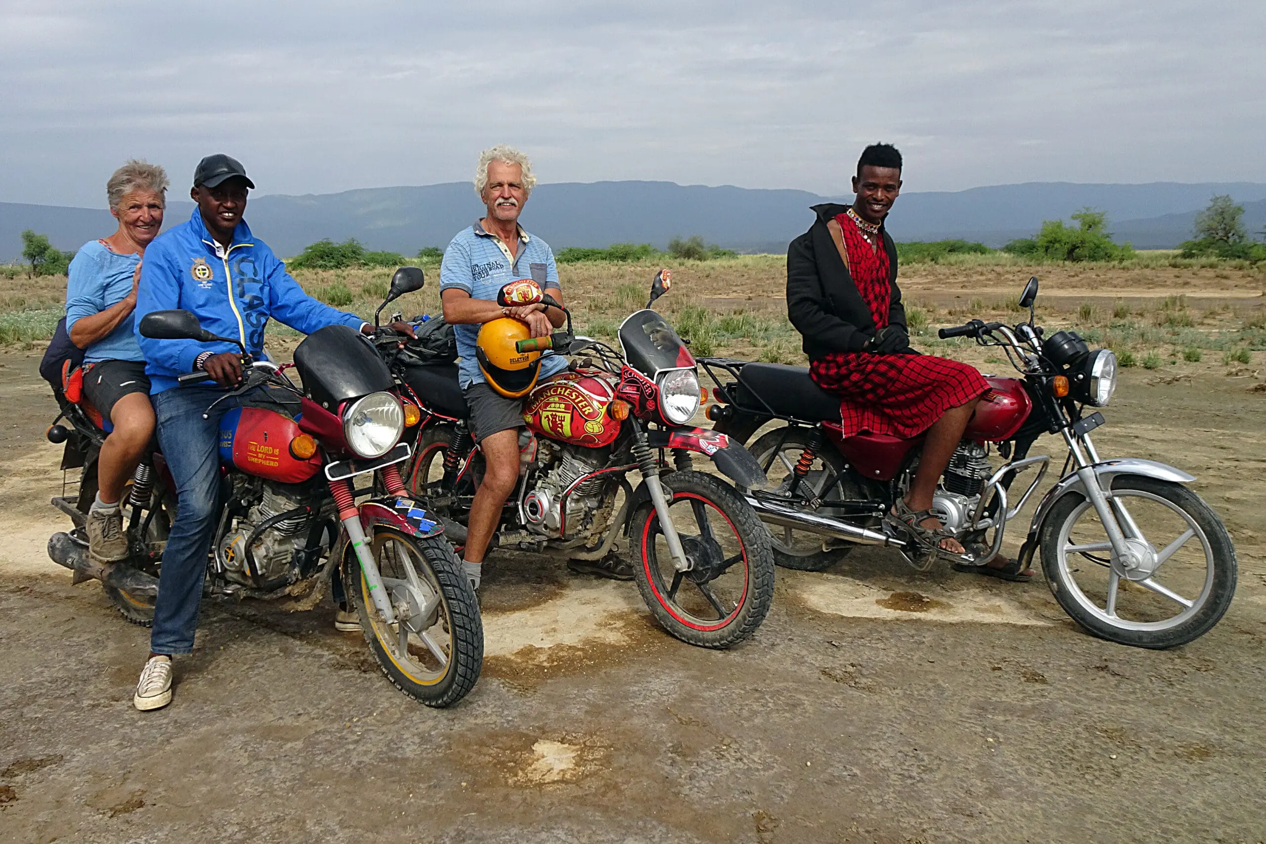 groep mensen op motoren met locals op open vlakte met bergen op achtergrond in kenia