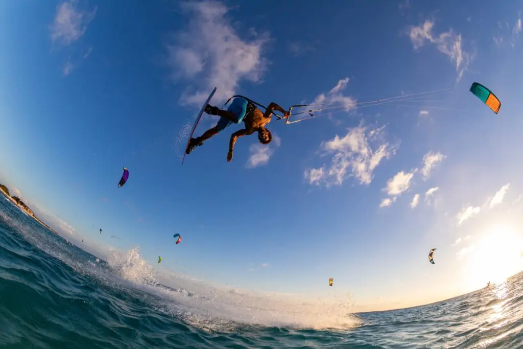 A kitesurfer performs an aerial trick above the ocean in South Africa as colorful kites and fellow surfers fill the background under a bright, blue sky—an unforgettable highlight while travelling.