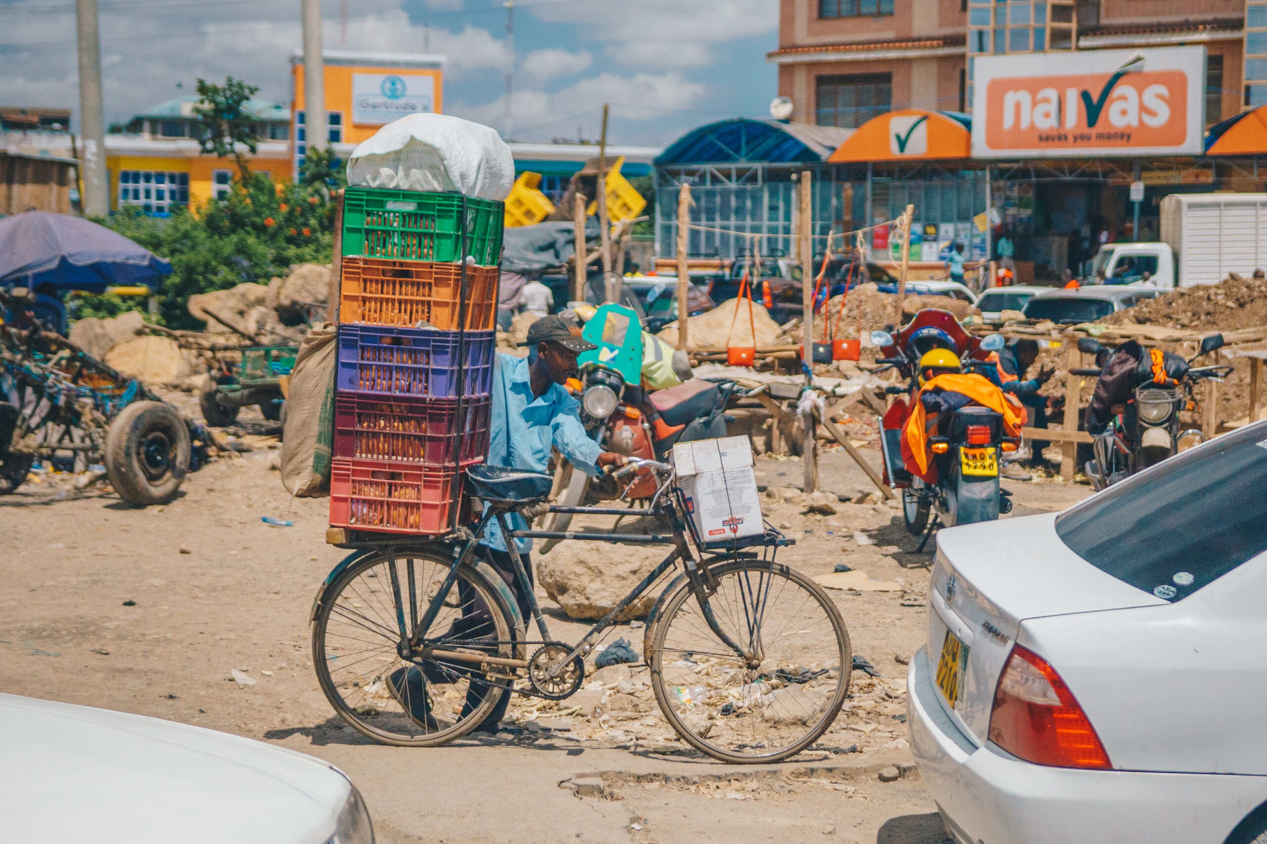 man met fiets vol kleurrijke kratten voor Naivas supermarkt in Kenia