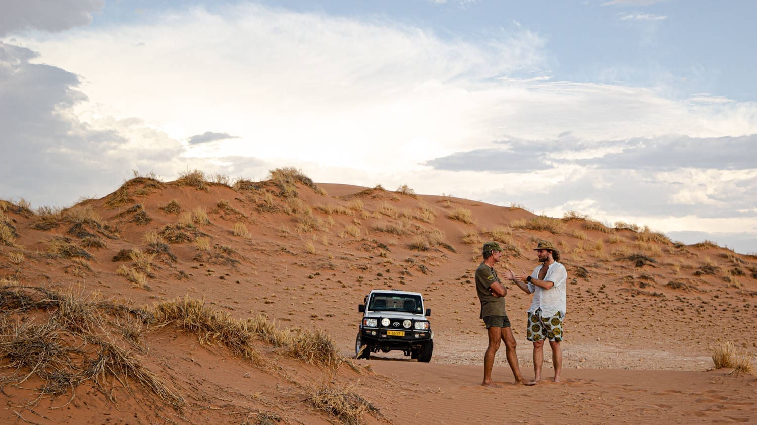 twee mannen staan pratend voor jeep in rood zandduinlandschap in namibië