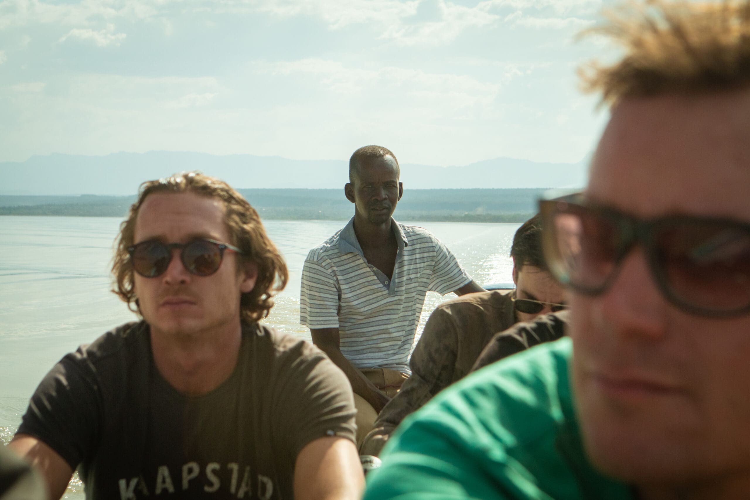 Een groep reizigers zit in een boottocht op Lake Baringo met een lokale gids aan het roer en uitzicht over het meer en de heuvels
