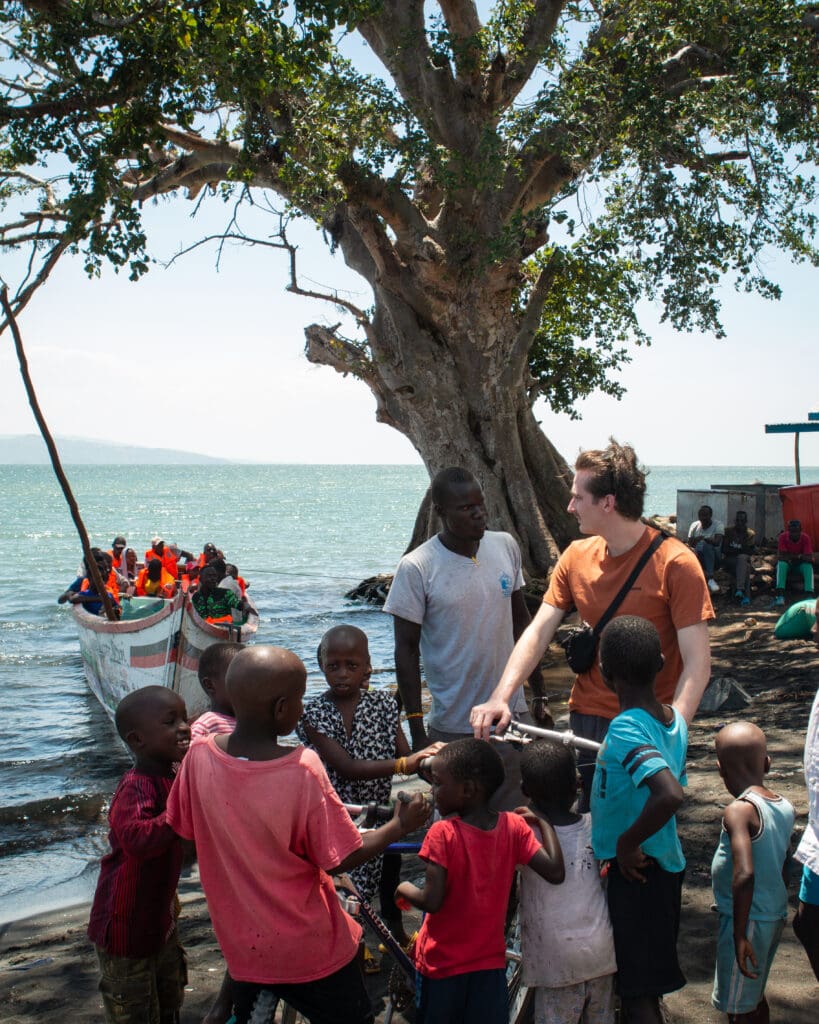 groep kinderen en volwassenen bij het meer van victoria terwijl een boot met mensen aanmeert in kenia