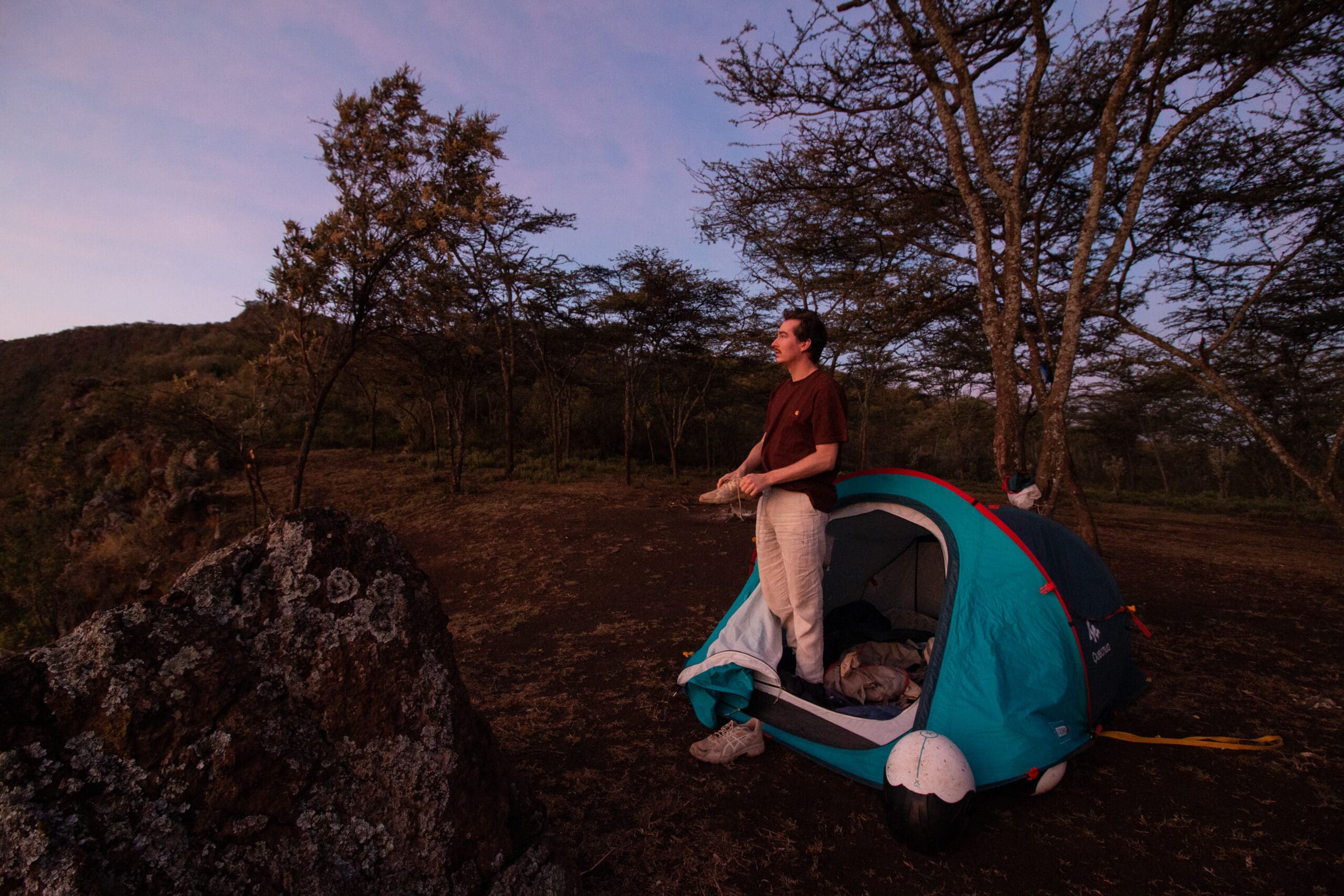 Kampeerder staat naast een tent in de bossen van Mount Suswa tijdens zonsondergang