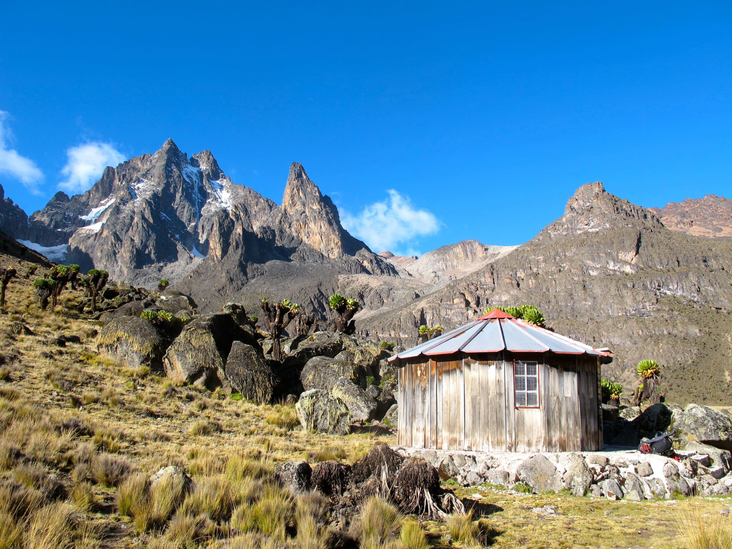 Houten berghut aan de voet van Mount Kenya met besneeuwde pieken en blauwe lucht op de achtergrond