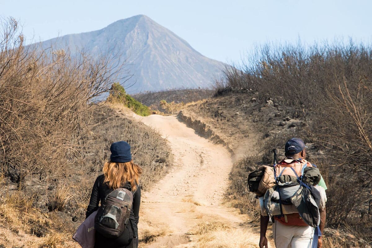 Twee wandelaars lopen met backpacks over een stoffig pad richting Mt Kenya