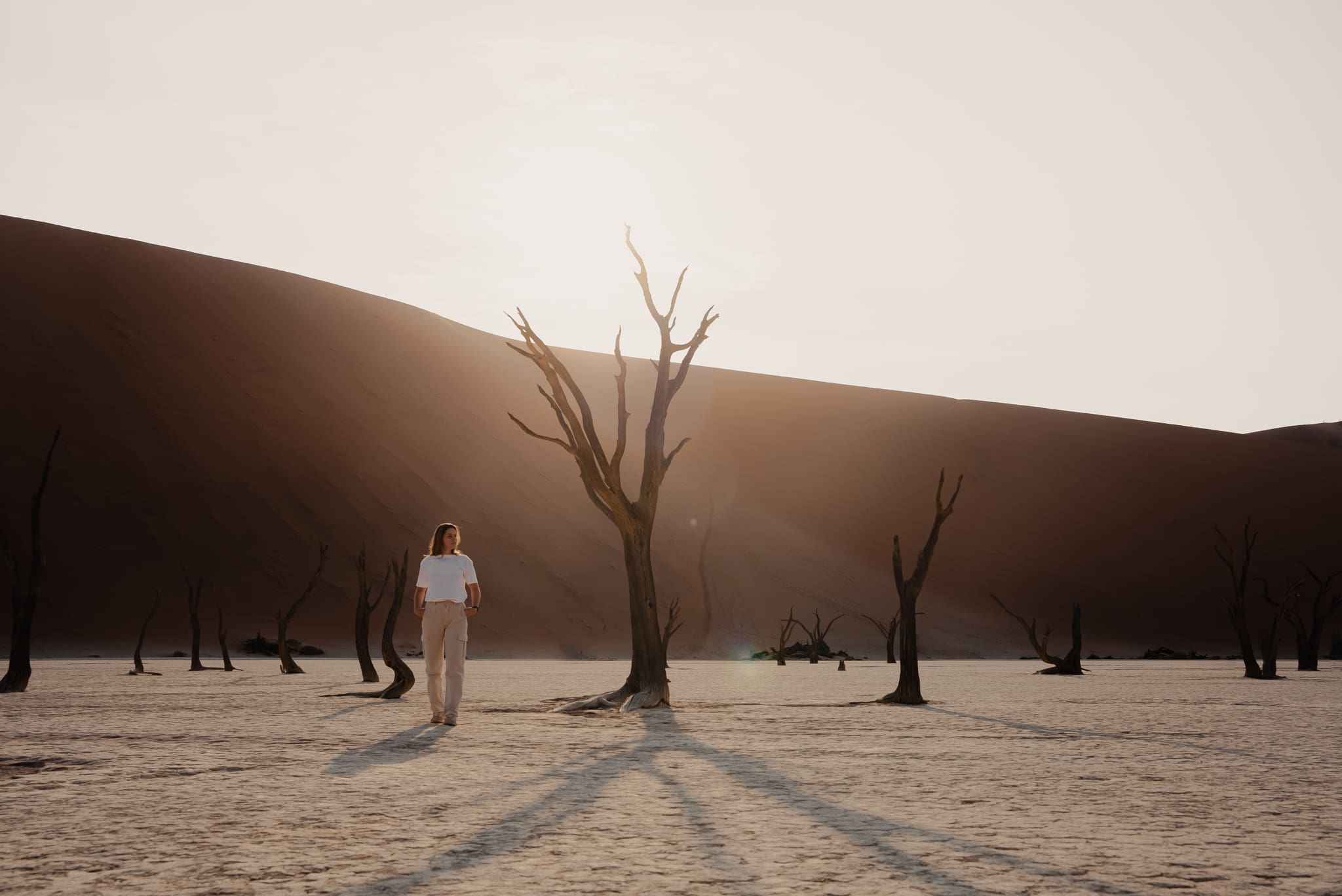 vrouw loopt tussen dode bomen in droog zoutpanlandschap bij zonsondergang in namibië door hannahninavr