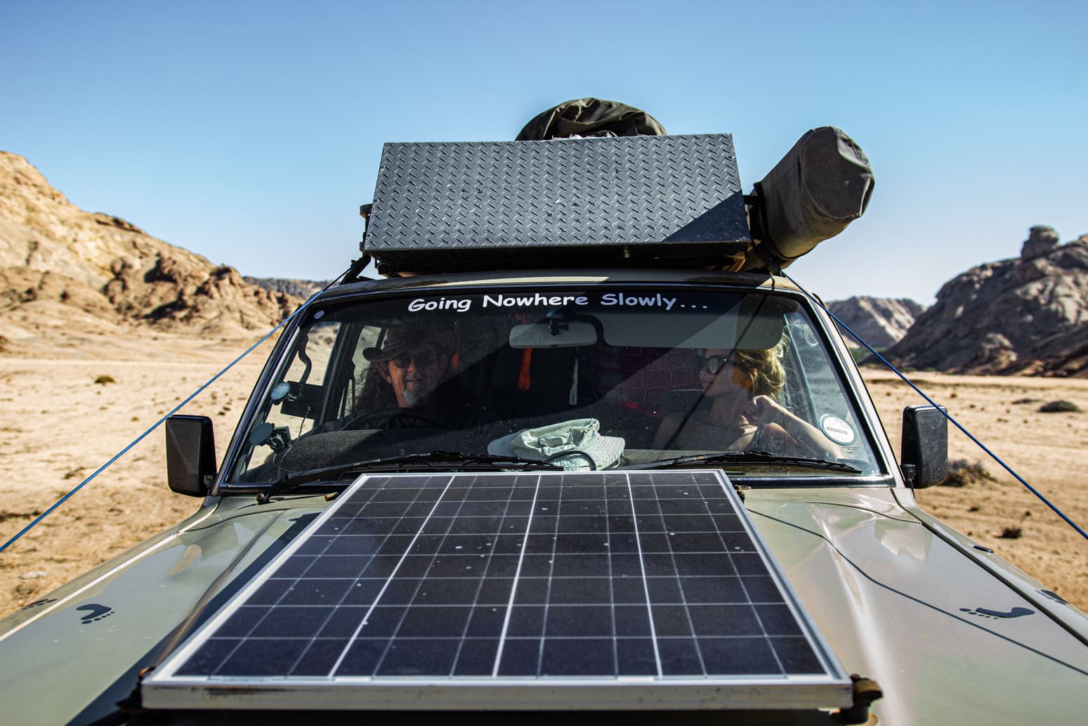 terreinwagen met zonnepaneel op de motorkap geparkeerd in een rotsachtig woestijnlandschap in namibië
