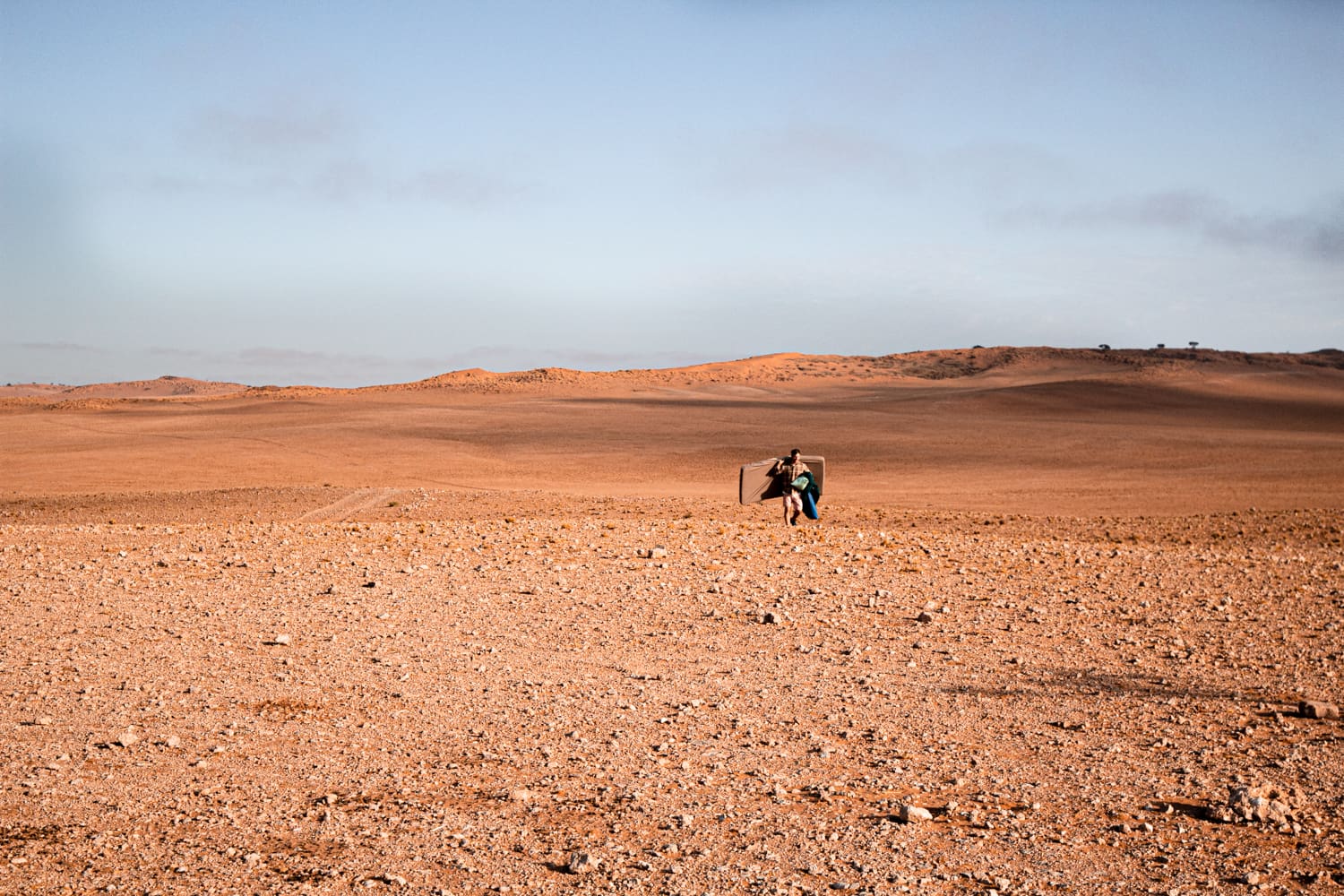 een wandelaar loopt met kampeeruitrusting over de kale rotsbodem van een uitgestrekt woestijnlandschap in namibië