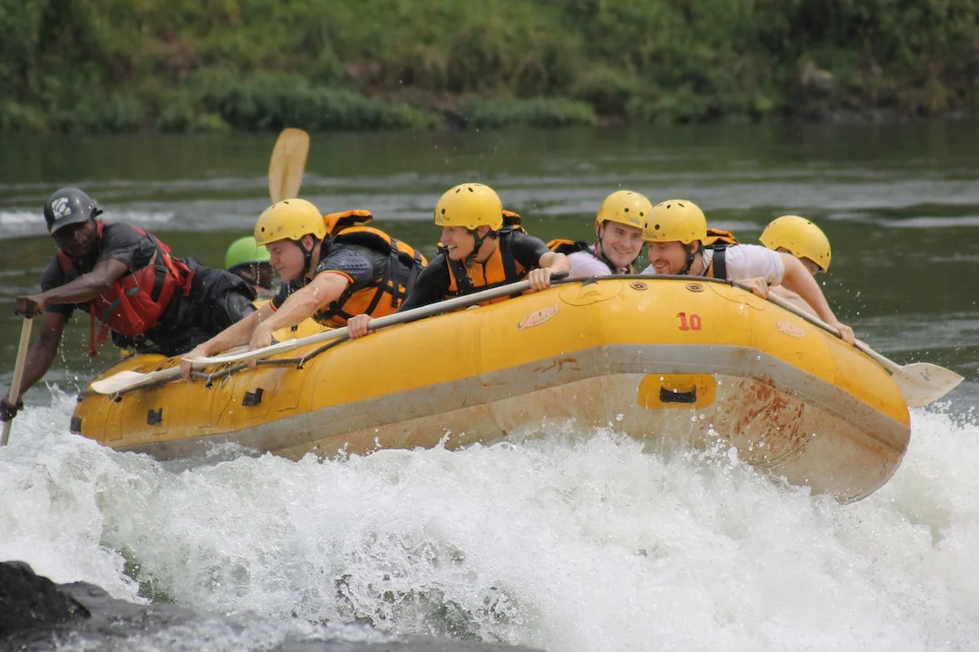 Zes mensen met gele helmen en reddingsvesten varen in een geel opblaasbaar vlot door wildwater, terwijl een gids naast hen peddelt en het water om hen heen opspat.