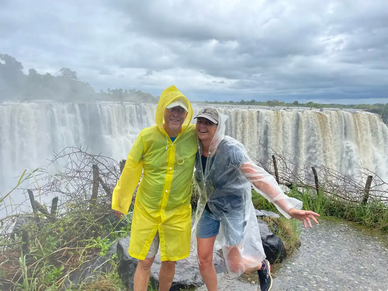Een man in een gele regenjas en een vrouw in een doorzichtige poncho poseren voor een grote waterval.