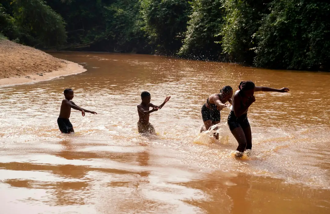 Vier kinderen die spelen en spetteren in een ondiepe rivier met bruin water.