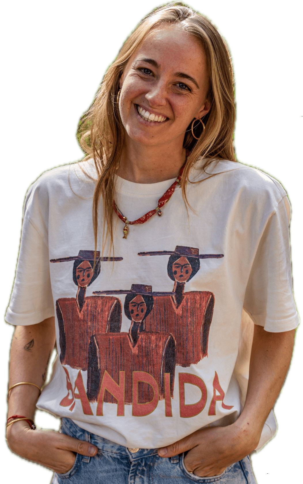 Een vrouw die glimlacht terwijl ze een crèmekleurig T-shirt draagt met een afbeelding van drie figuren met hoeden en het woord BANDIDA onderaan gedrukt.