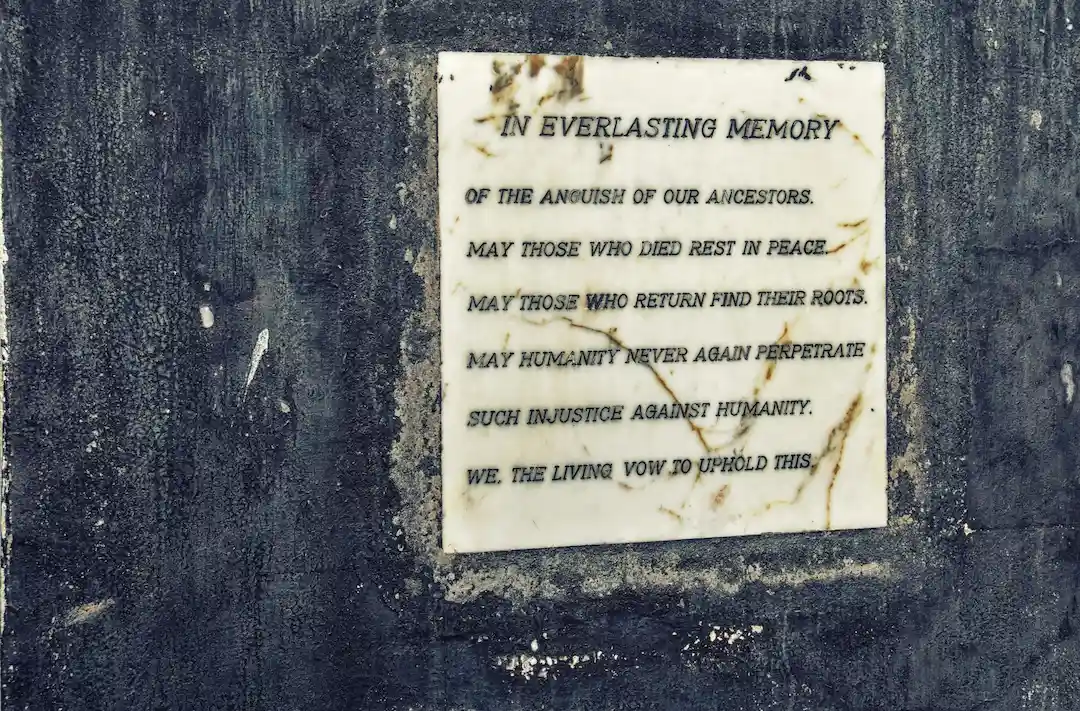 Een stenen gedenkplaat die in een donkere muur is ingebouwd, met een inscriptie ter ere van de voorouders en een belofte om gerechtigheid hoog te houden.
