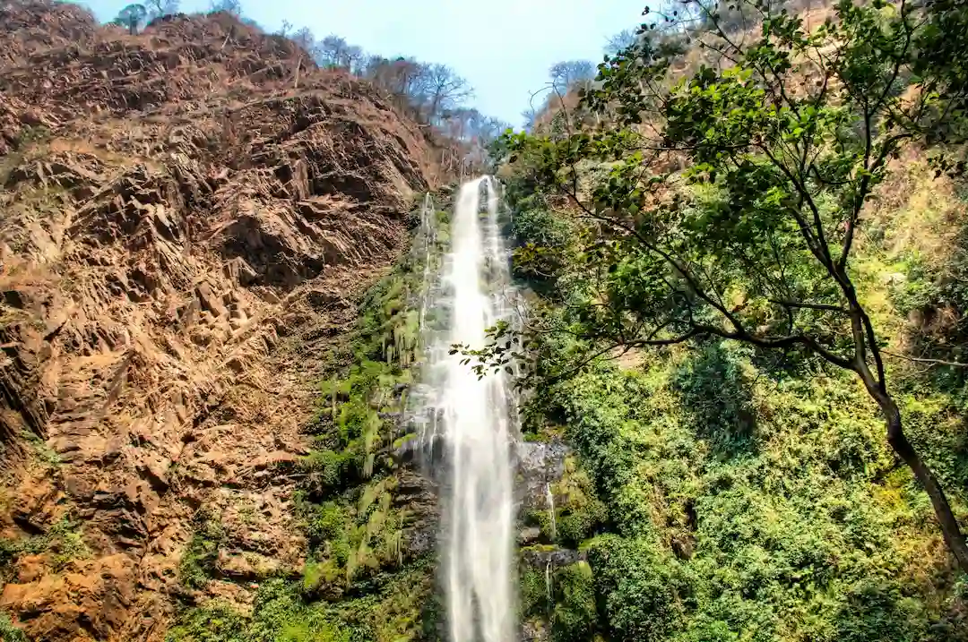 Een hoge, smalle waterval stort zich naar beneden langs een rotsachtige klif die begroeid is met groene vegetatie.