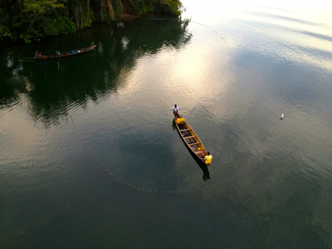 Luchtfoto van twee houten vissersboten op rustig water, met op elke boot twee mensen die een cirkelvormig net uitzetten.