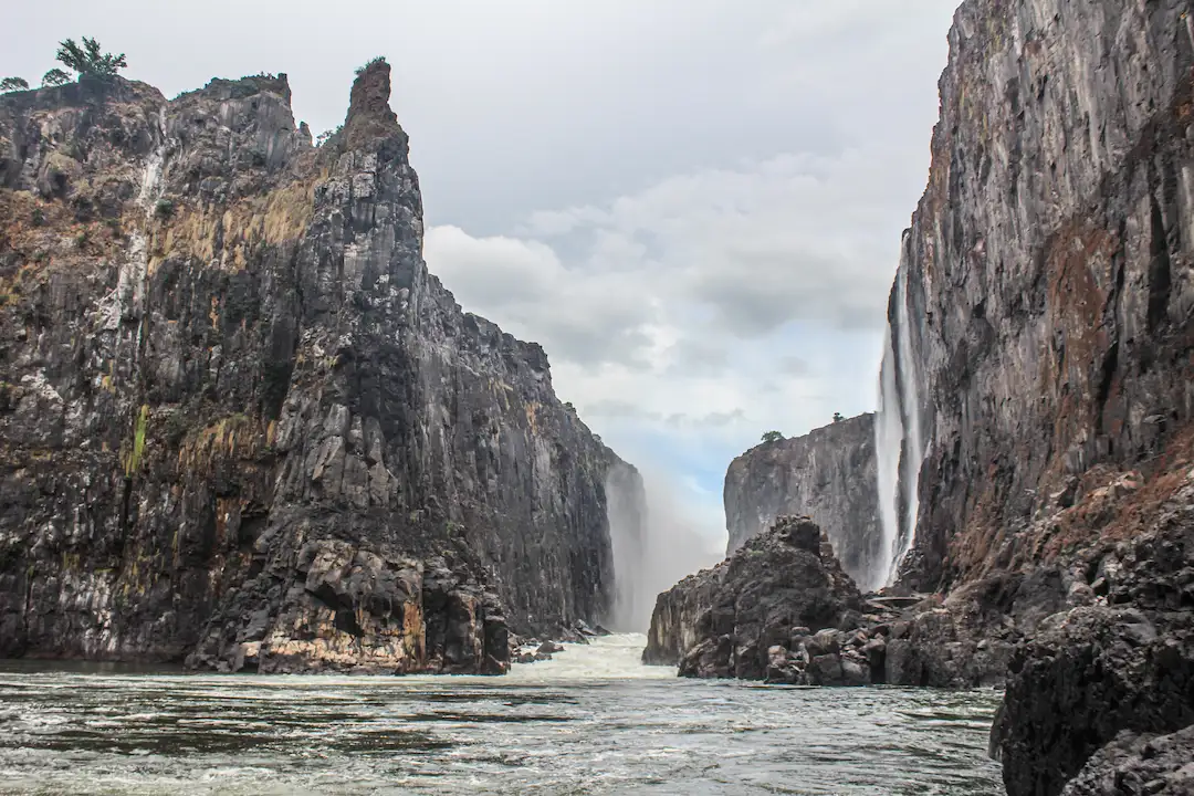 Een waterval stroomt tussen torenhoge, ruige rotswanden door en mondt uit in een rivier.